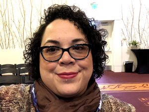 A portrait of a smiling woman with short curly hair and glasses.