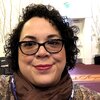 A portrait of a smiling woman with short curly hair and glasses.